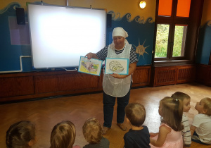 nauczycielka w stroju piekarza pokazuje dzieciom obrazki dotyczące produkcji chleba